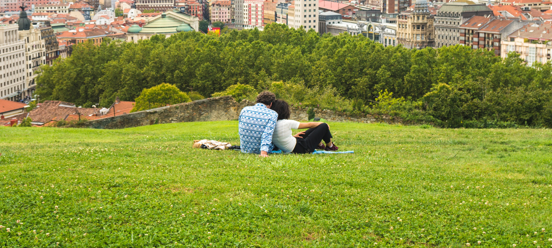 Pareja viendo una hermosa vista panorámica de Bilbao sentada en el parque de la colina sobre el Casco Antiguo Pareja viendo una hermosa vista panorámica de Bilbao sentada en el parque de la colina sobre el Casco Antiguo