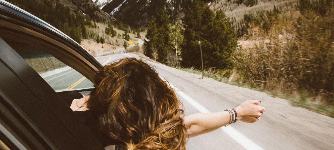Chica se asoma por la ventanilla de un coche en una carretera de montaña Chica se asoma por la ventanilla de un coche en una carretera de montaña