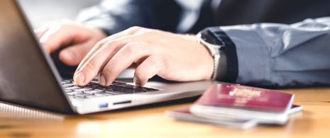 Persona che usa il computer con in primo piano il suo passaporto.